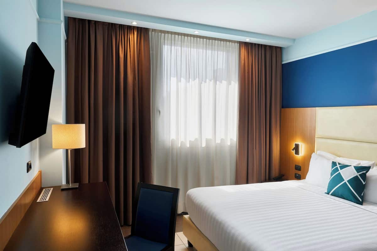 Una habitación de hotel con cama, escritorio, silla, televisor y cortinas.