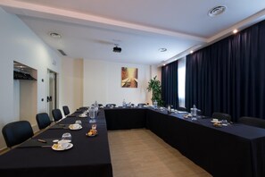 Un salón de conferencias con una larga mesa, sillas y una pantalla para proyector.