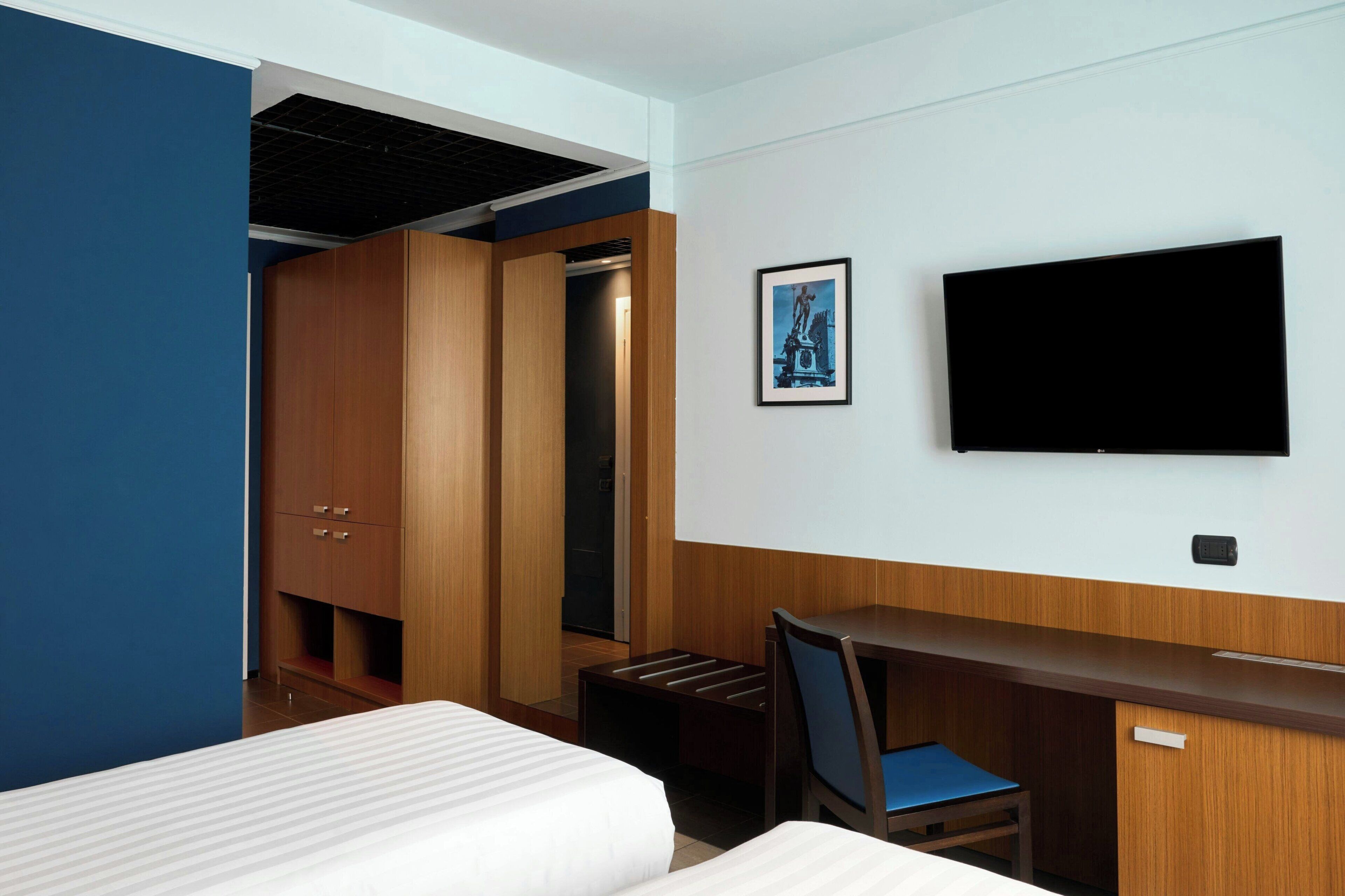 A hotel room with a bed, a desk, a chair, a TV, and a wardrobe.