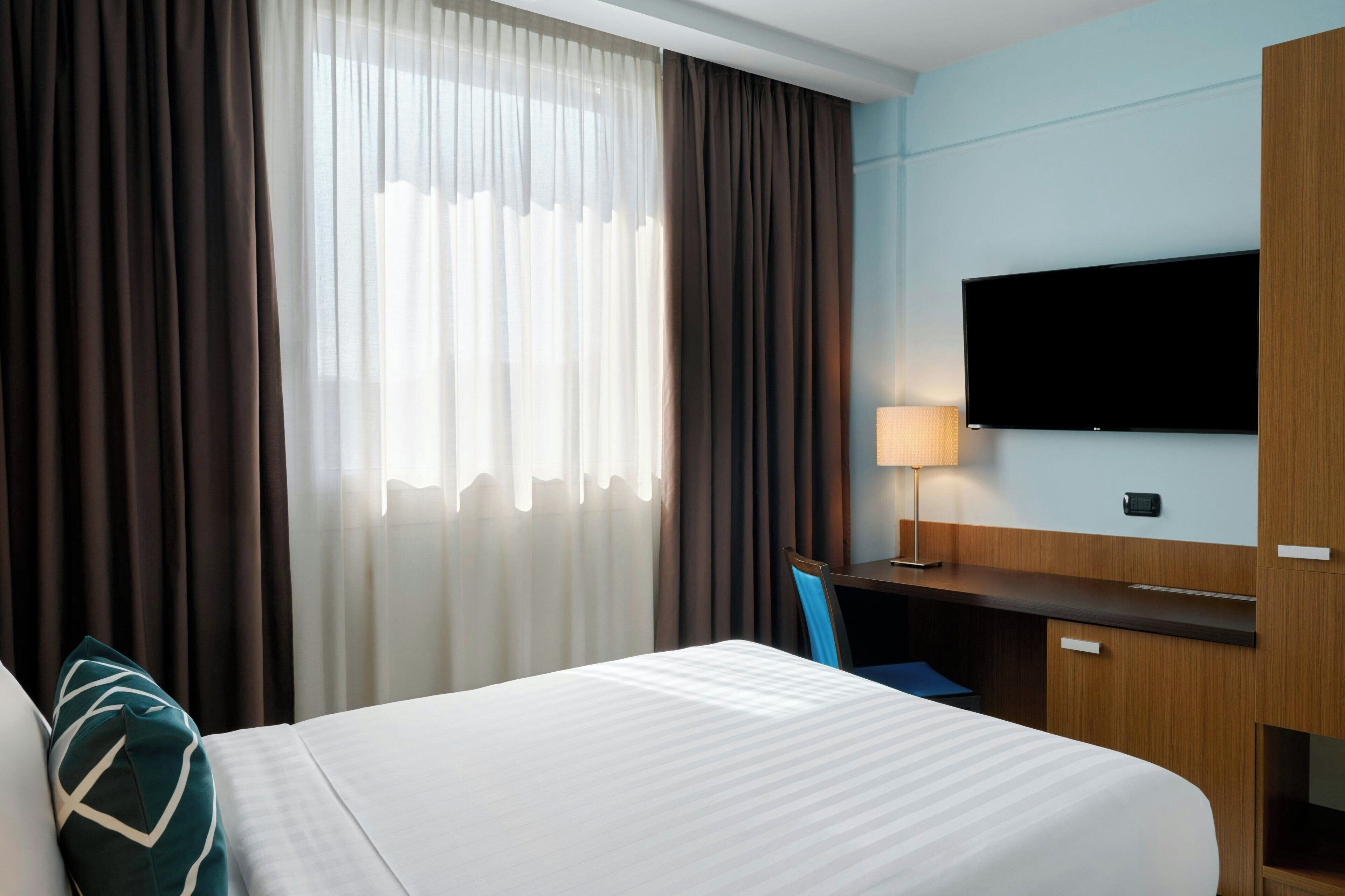 Ein Hotelzimmer mit Bett, Schreibtisch, Stuhl, Fernseher und Vorhängen.