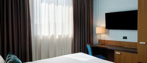 Ein Hotelzimmer mit Bett, Schreibtisch, Stuhl, Fernseher und Vorhängen.
