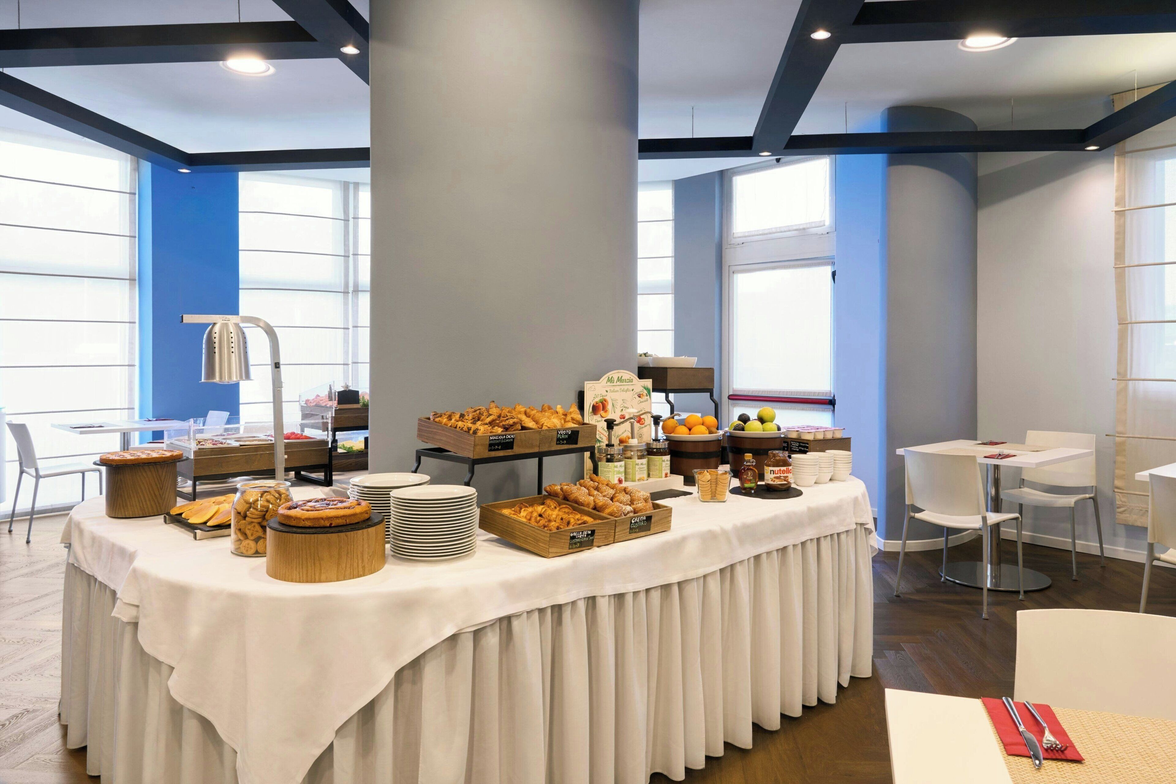 A buffet setup with various food items and a coffee station, surrounded by tables and chairs in a modern interior.