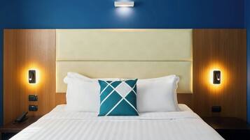 Une chambre d’hôtel avec un grand lit, deux tables de chevet, une tête de lit et des lampes fixées au mur.