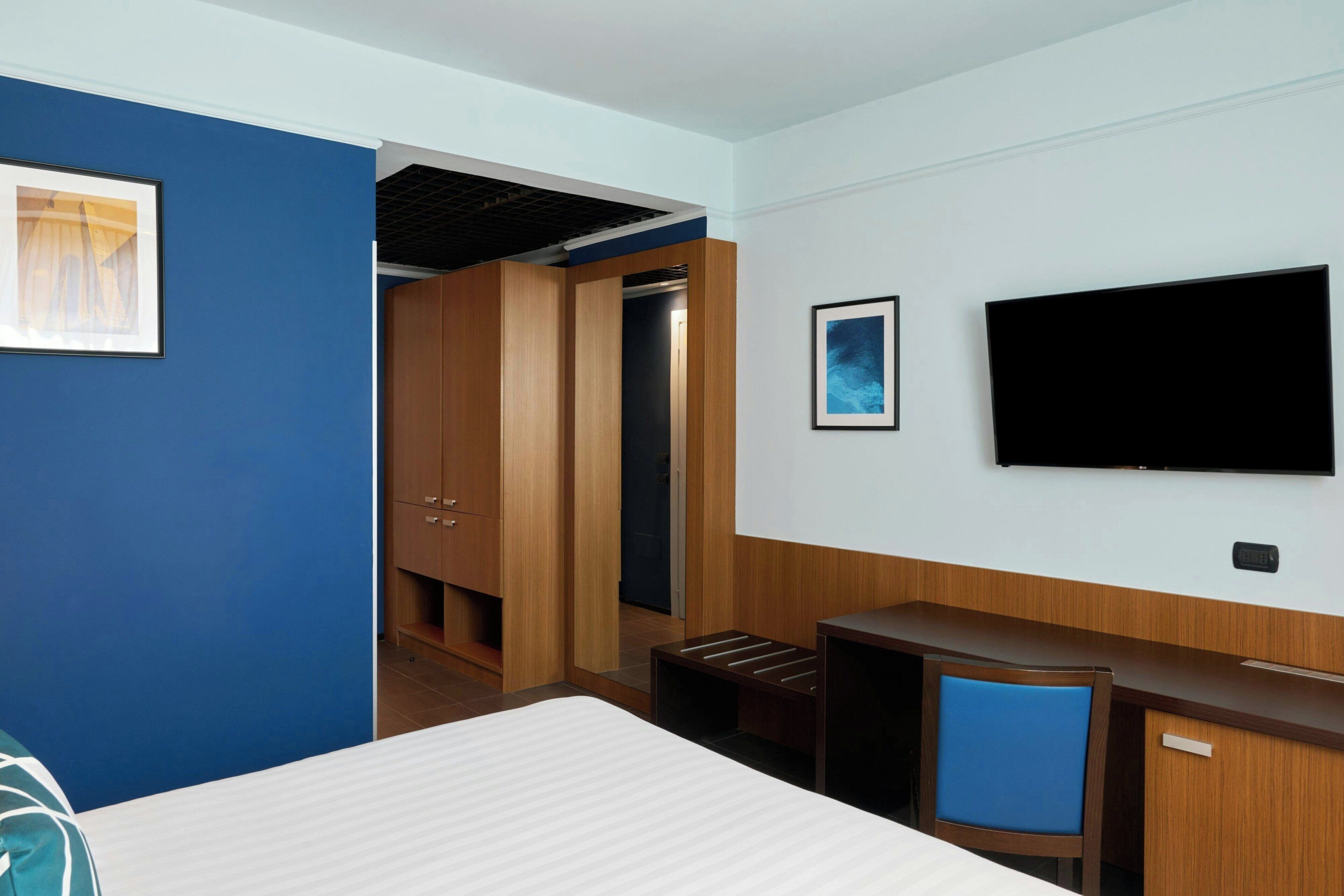Una habitación de hotel con cama, escritorio, televisor y armario.