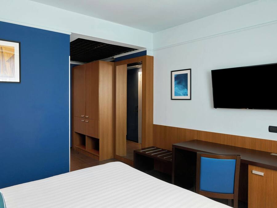 Una habitación de hotel con cama, escritorio, televisor y armario.