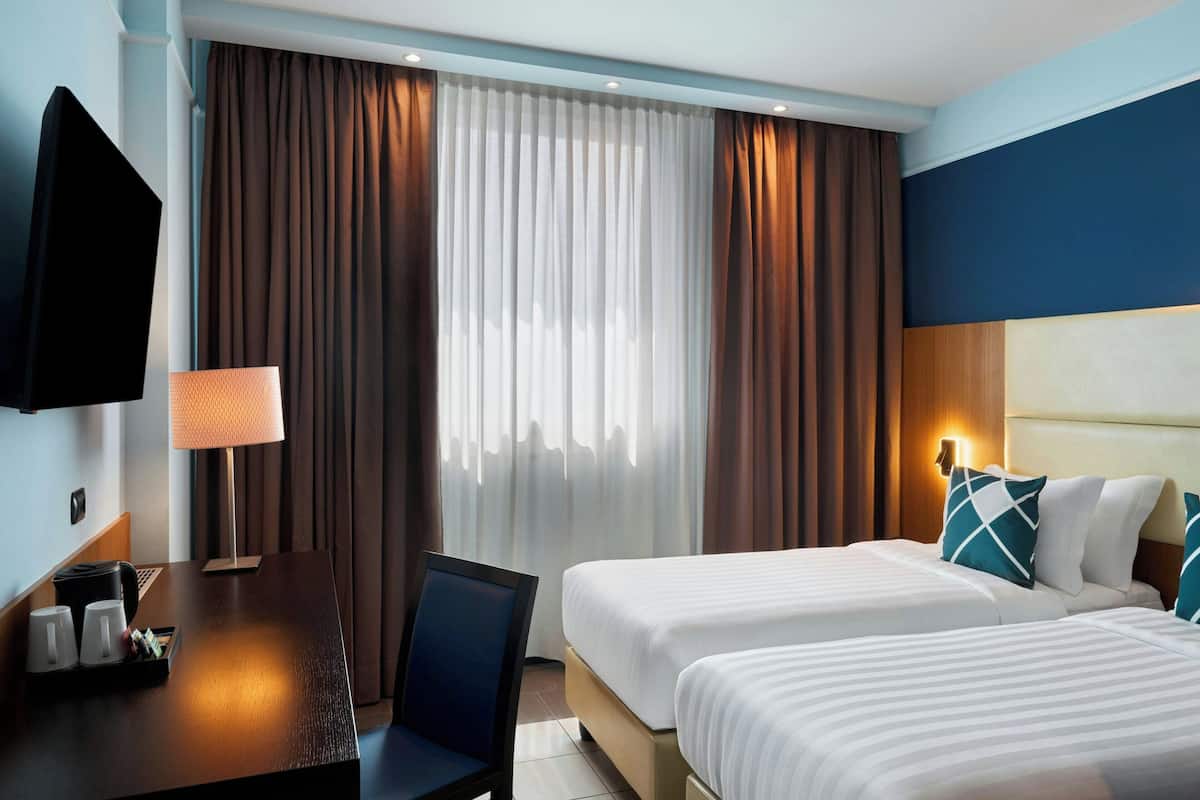 Habitación de hotel con dos camas, un escritorio con lámpara, televisión y ventana con cortinas.