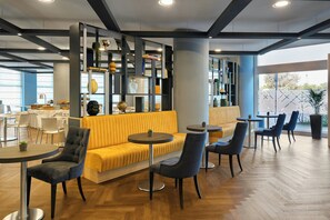 Un área de estar moderna con un sofá amarillo, sillas oscuras y un suelo de madera en espiga.
