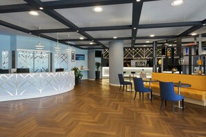 Een moderne receptie met een gebogen bureau, blauwe stoelen, een bar en een zithoek met een gele bank.