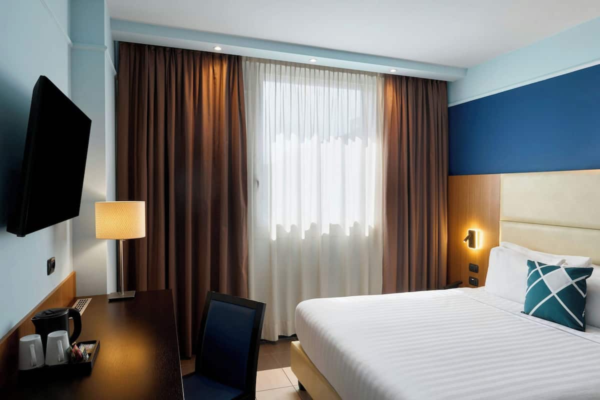 Una habitación de hotel con una cama, un escritorio con lámpara, un televisor y cortinas.