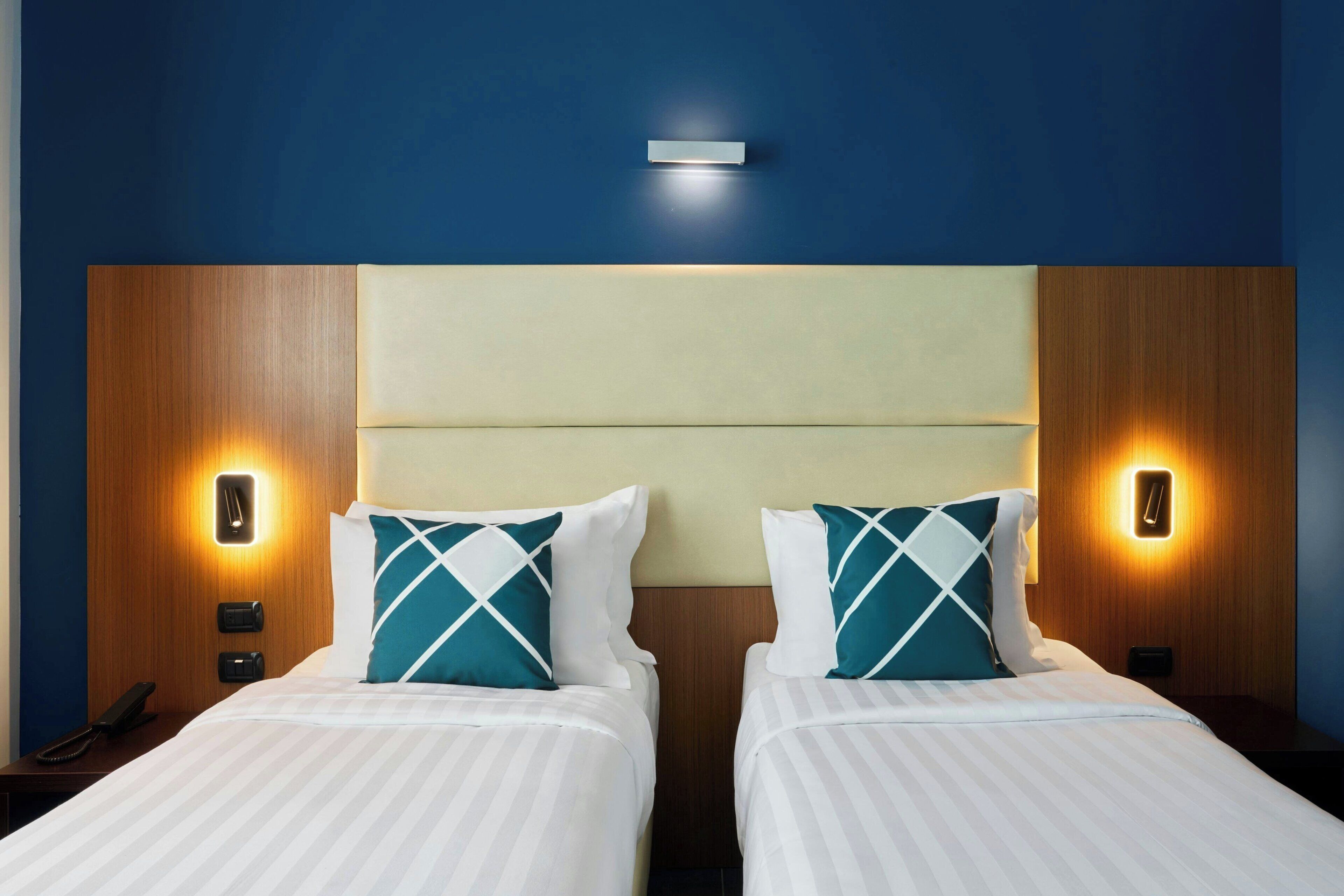 Habitación de hotel con dos camas, cada una con cabecera, lámparas de noche y teléfono en la mesita.