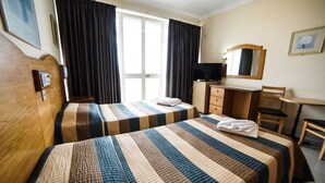 Habitación de hotel con dos camas, un escritorio, una silla, un televisor y una ventana con cortinas.
