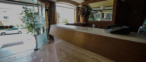 A hotel reception area with a counter, a potted plant, a telephone, and a view of the street outside.