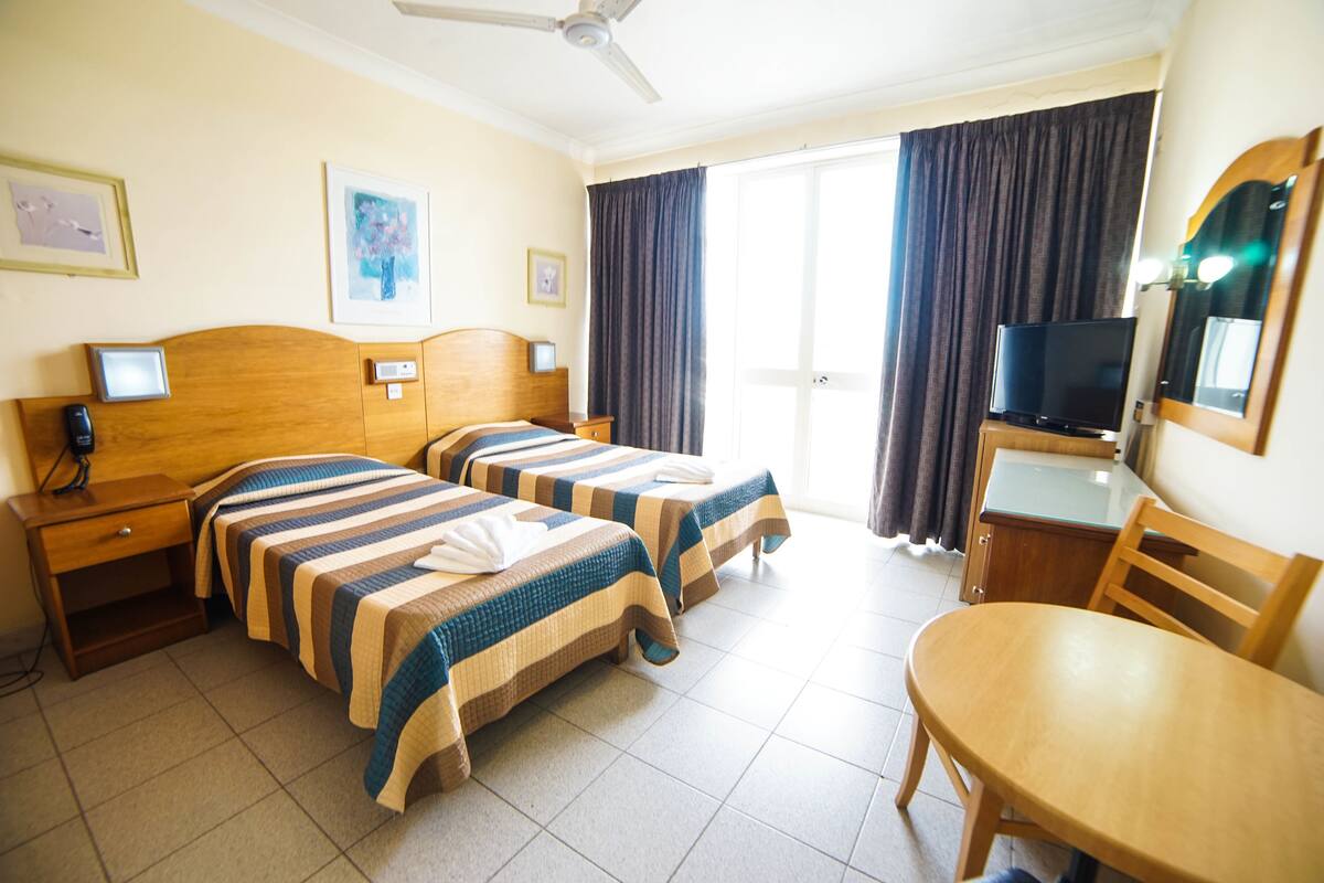 Hotellihuone, jossa on kaksi sänkyä, televisio, työpöytä ja tuoli.