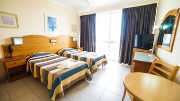 A hotel room with two beds, a desk, a chair, a television, and a ceiling fan.