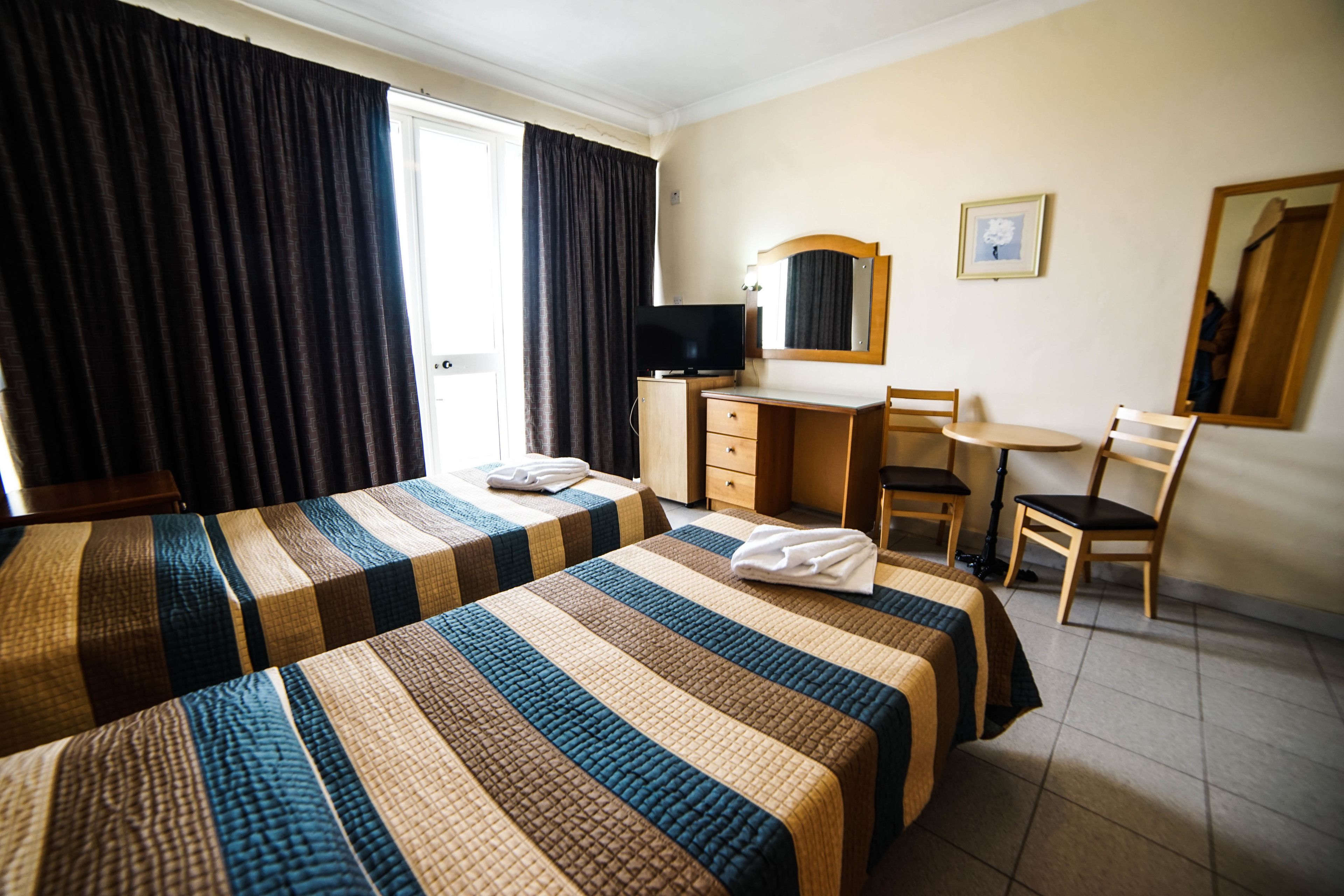 Una habitación de hotel con dos camas, un escritorio, una silla, un televisor y un espejo.