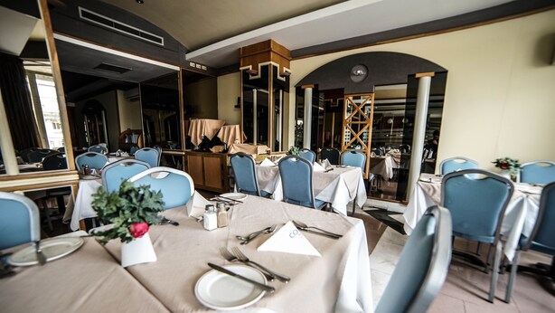 Un restaurante con mesas dispuestas para comer, sillas azules y un espejo grande que refleja el interior.
