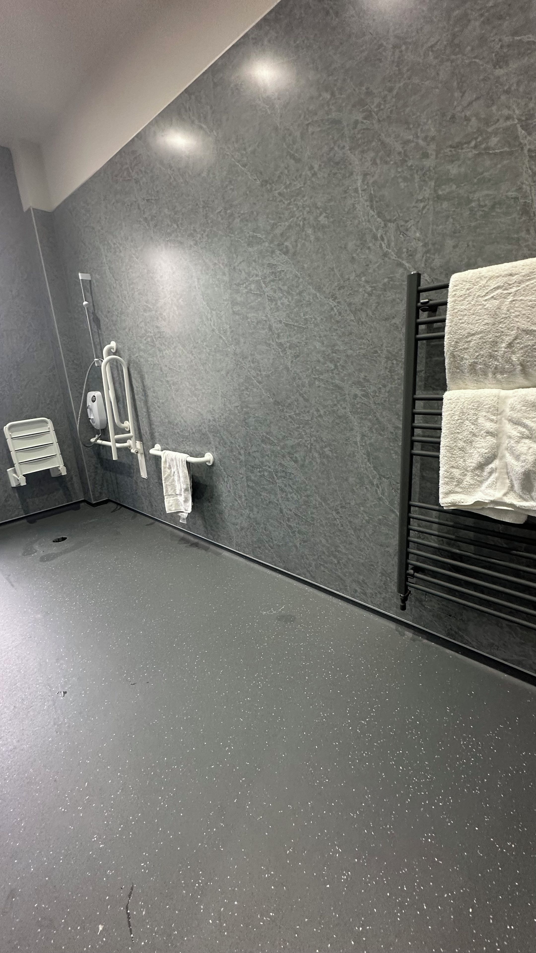 A modern bathroom with a grey marble wall, a black towel rack, and a white towel hanging.