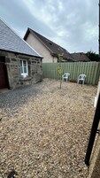 A stone building with a sloped roof, a gravel driveway, and a wooden fence.