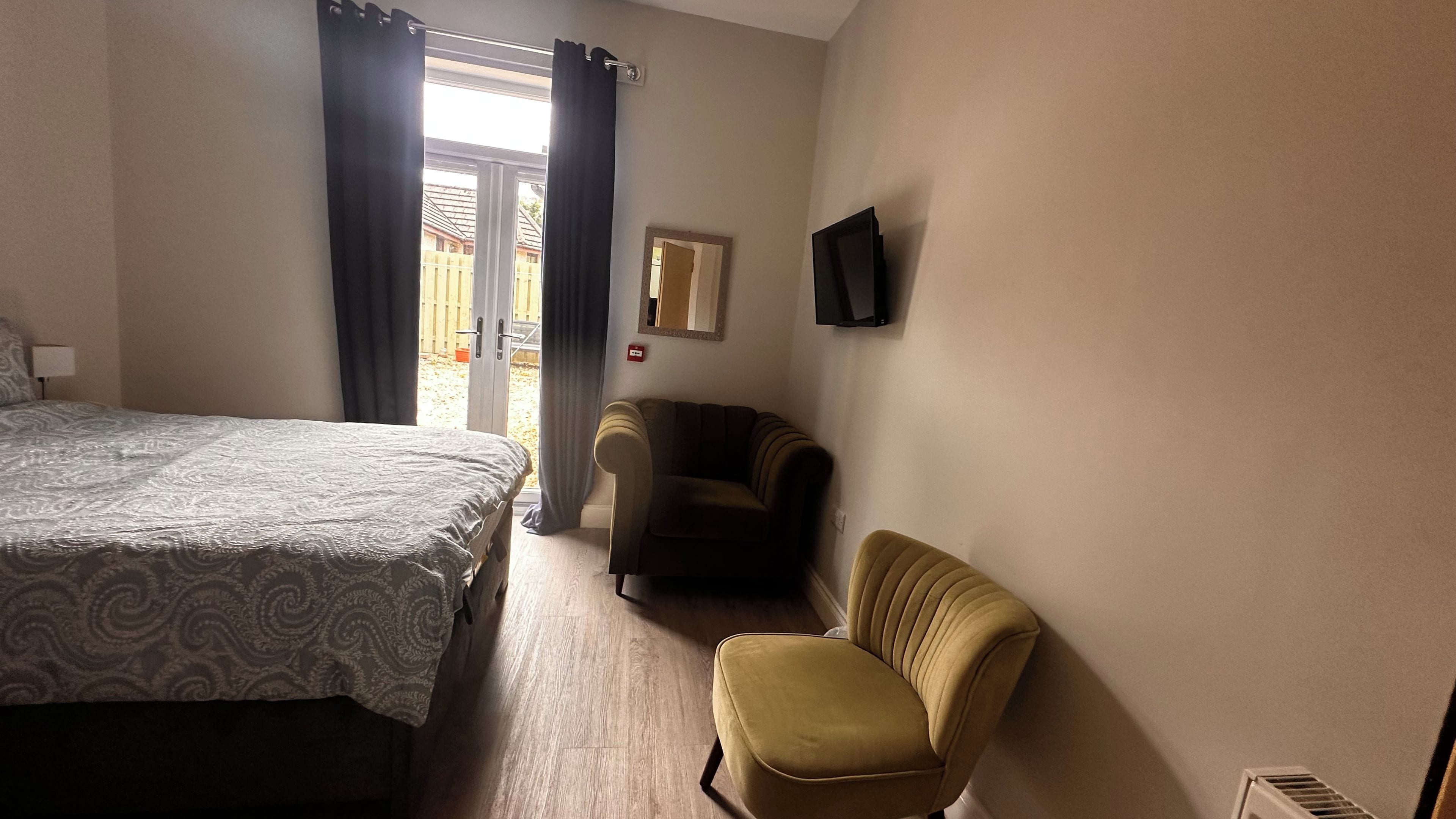 A hotel room with a bed, a chair, a television, and a sliding door leading to an outdoor area.