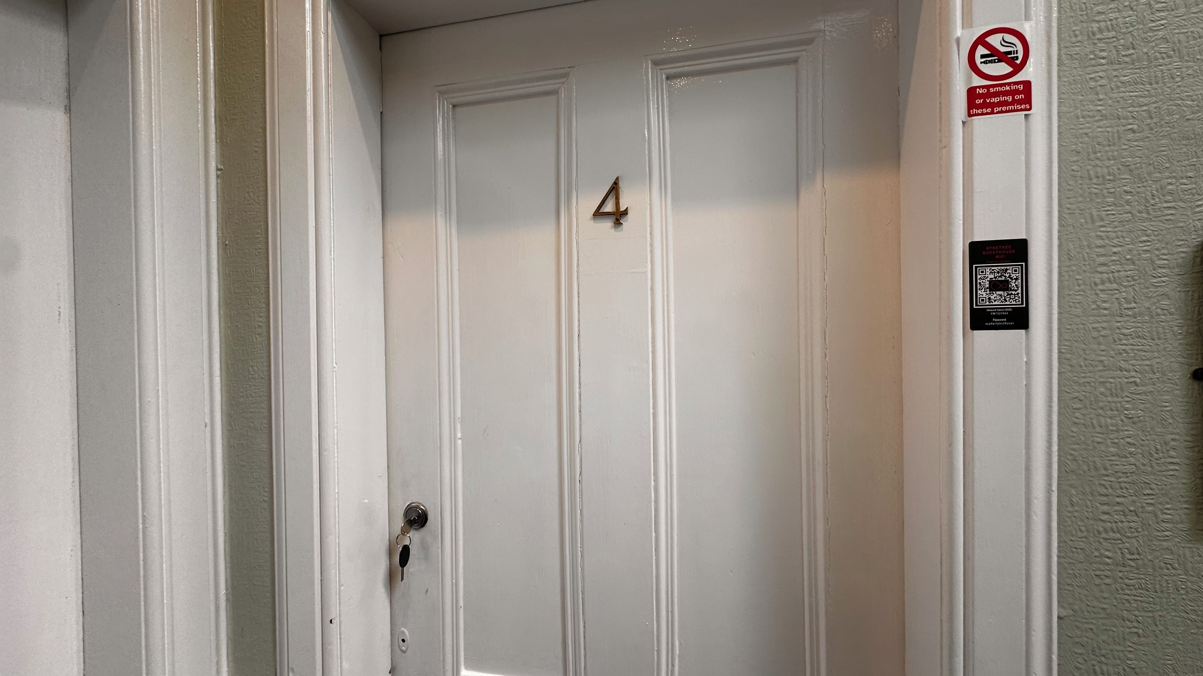 A white door with the number 4, a no-smoking sign, and a QR code for guesthouse information.