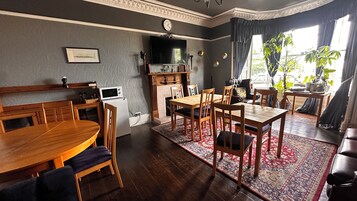 Een eethoek met een houten tafel en stoelen, een televisie boven de open haard en een klok aan de muur.