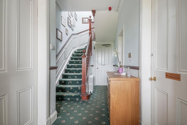 A hallway with a wooden staircase, a reception desk, and a sign indicating a dining room. - Aynetree Guest House (Edinburgh)