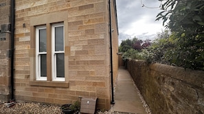 A stone building with a window, a pathway, and a stone wall with vegetation. - Aynetree Guest House (Edinburgh)