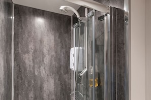 Une douche fermée par des parois en verre, dotée d’un pommeau de douche à main et d’un panneau de commande fixé au mur.