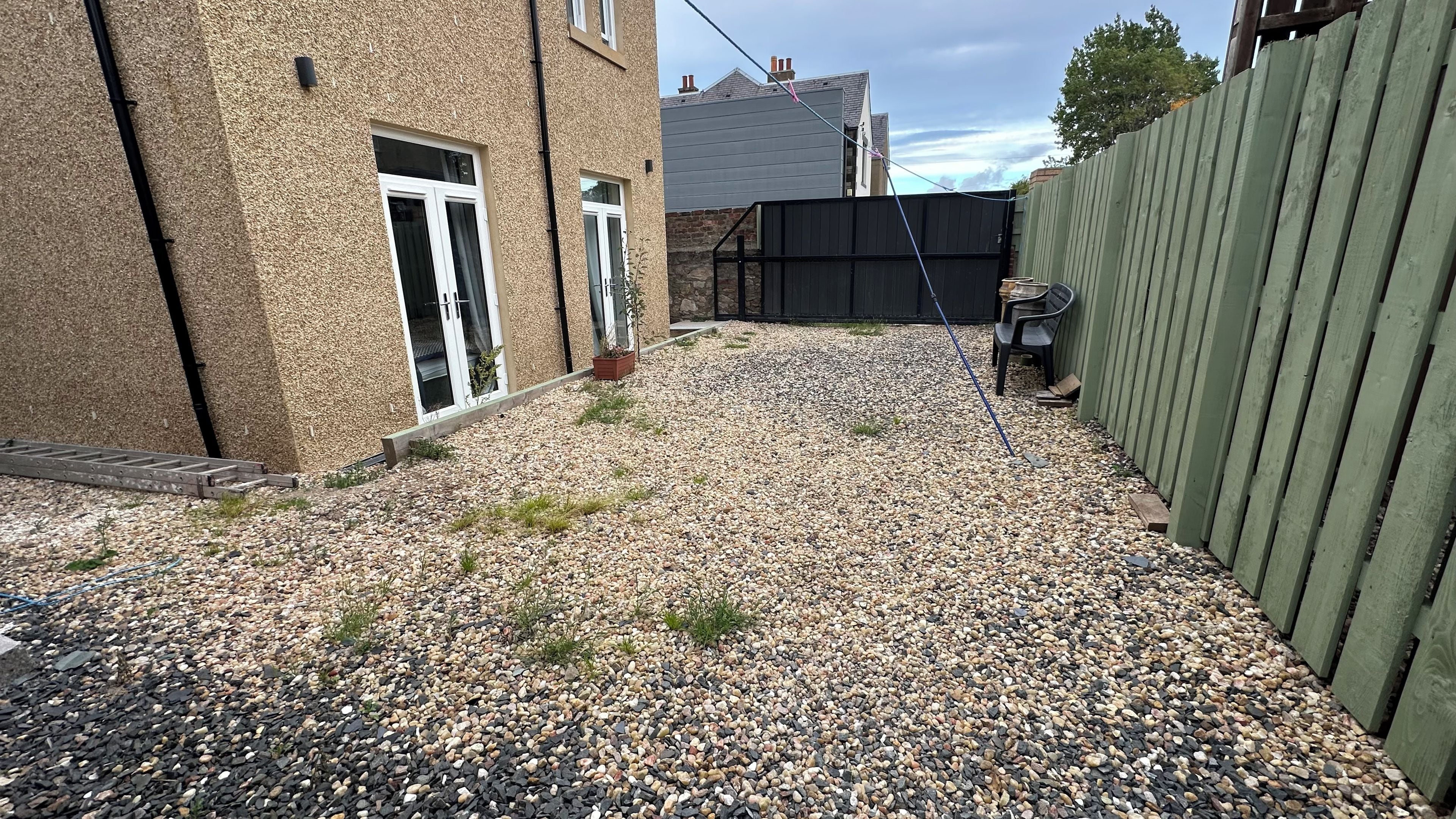 A gravel driveway leading to a house with a wooden fence and a metal gate.