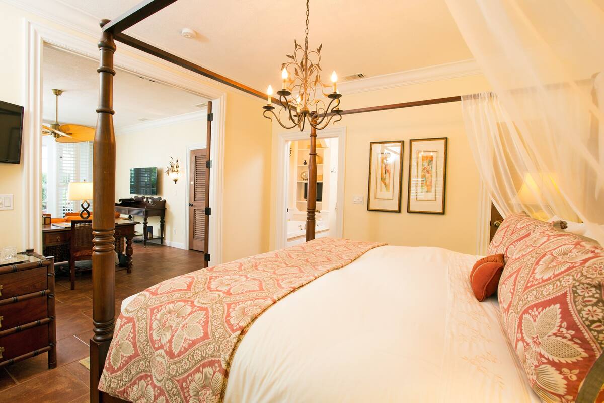 A bedroom with a four-poster bed, a chandelier, and a desk with a lamp.