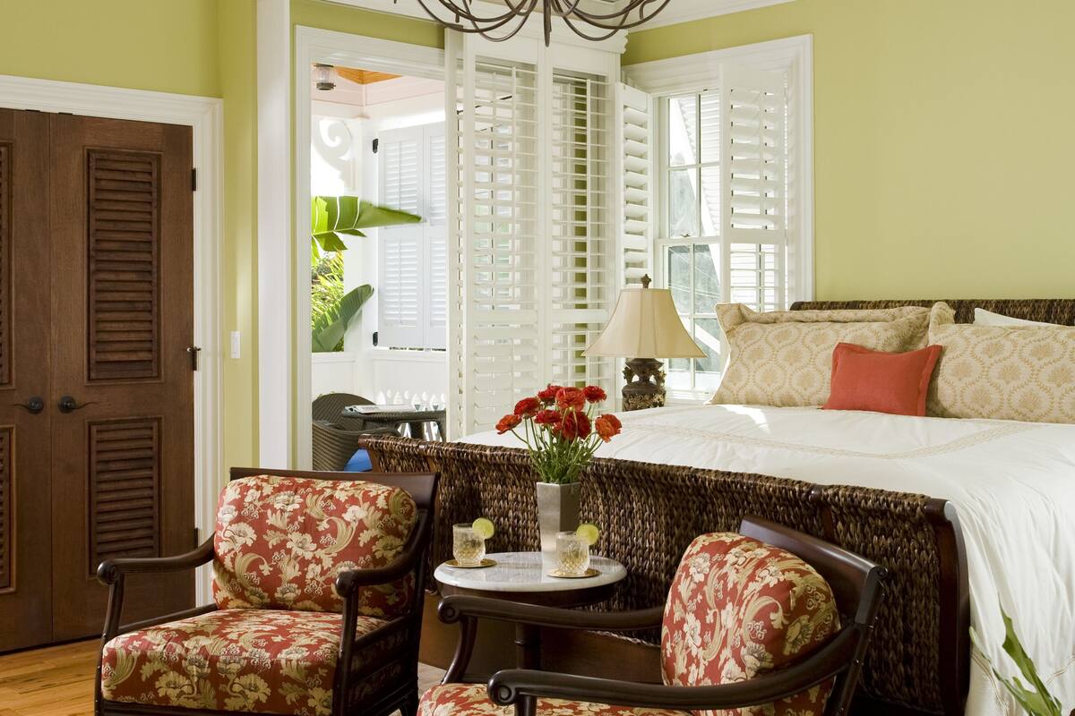 A bedroom with a large bed, two armchairs, a small table with a lamp, and a chandelier.