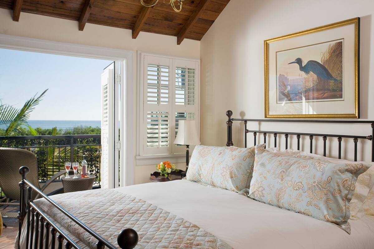 A bedroom with a bed, a balcony with a chair, and a view of the ocean.