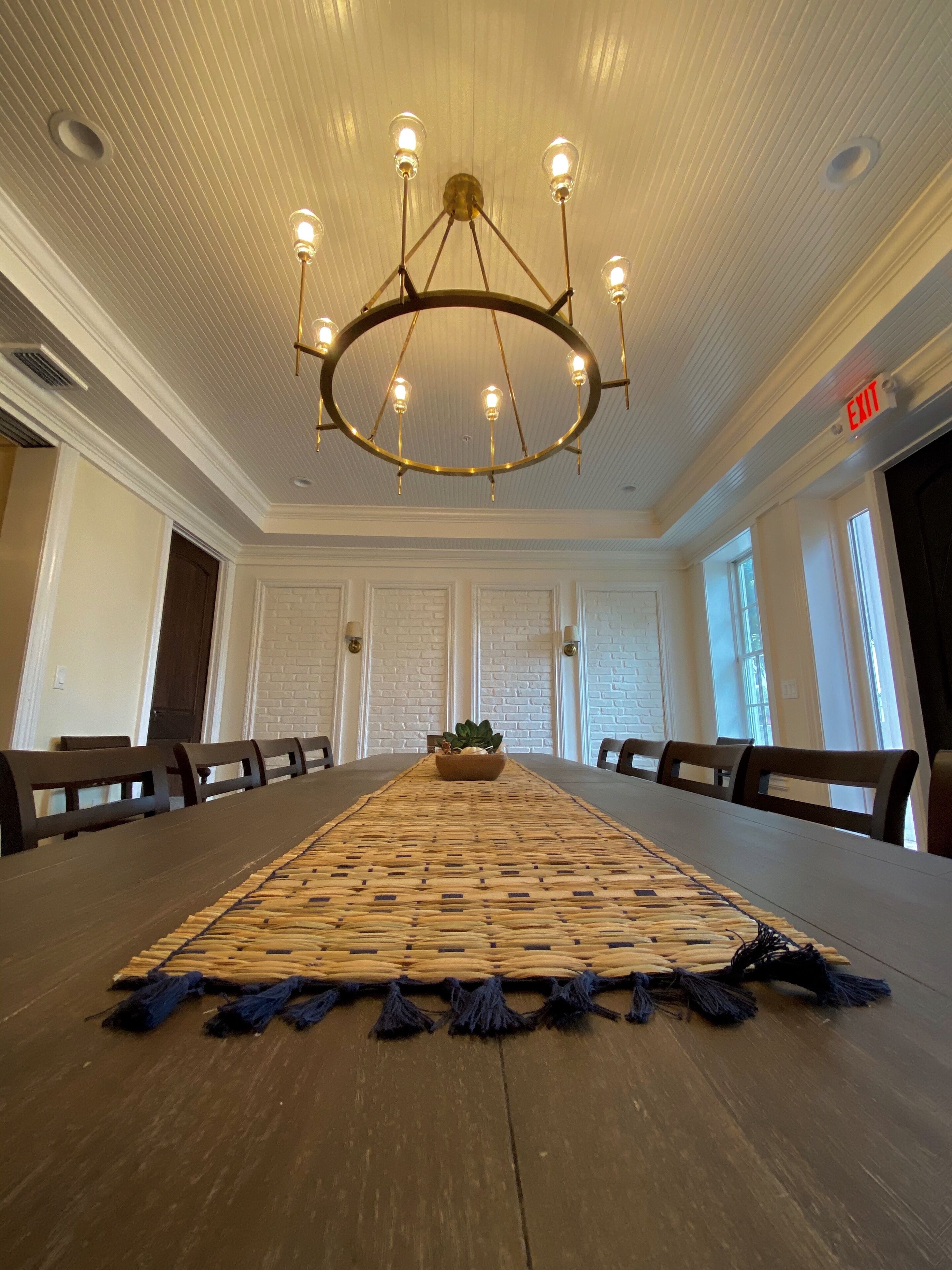 A conference room with a long table, chairs, a chandelier, and a potted plant.