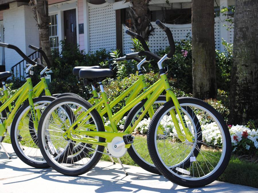 A row of yellow bicycles parked in front of a building with a white fence and greenery.