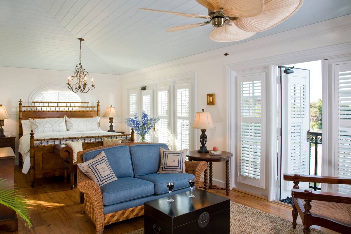 A bedroom with a wooden bed, a blue sofa, a chandelier, and a view through the window.
