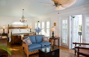 A bedroom with a wooden bed, a blue sofa, a chandelier, and a view through the window.