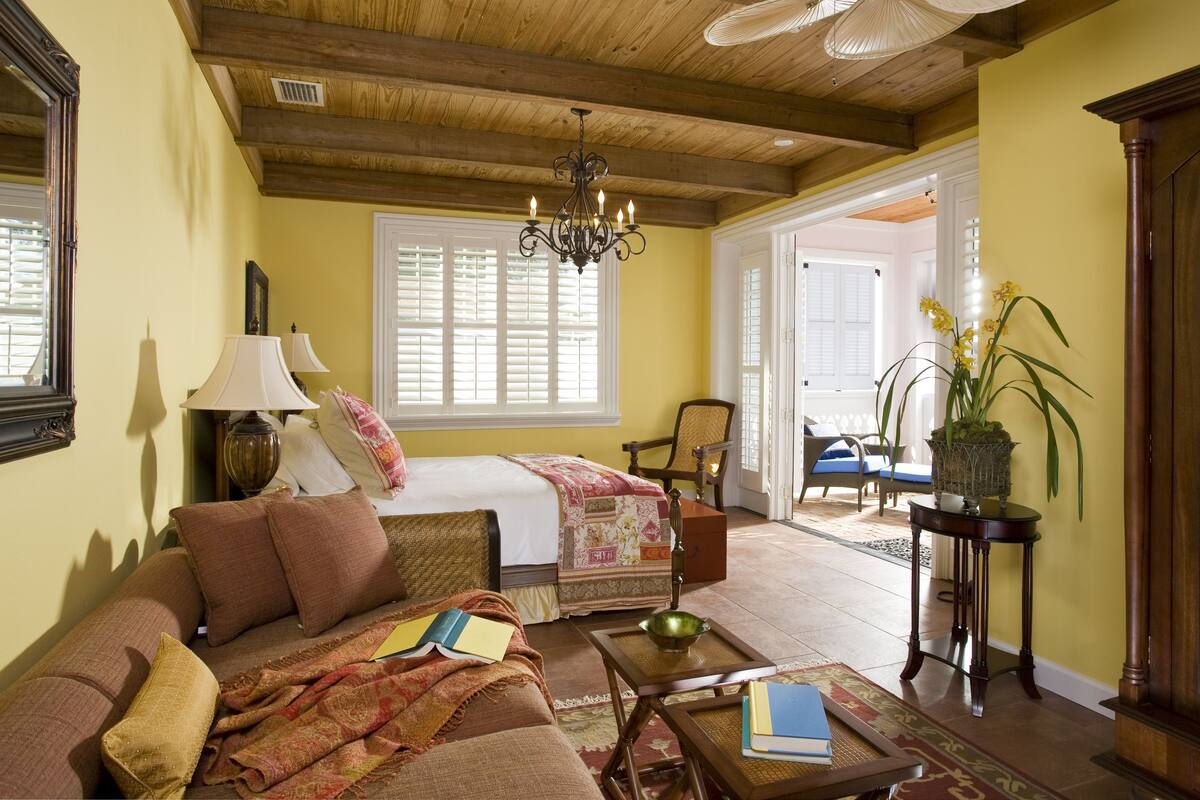 A cozy room with a bed, a sofa, a chandelier, and a view of the outside.