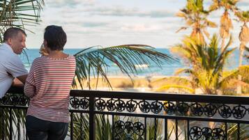 A couple standing on a balcony overlooking a beach with palm trees and the ocean.