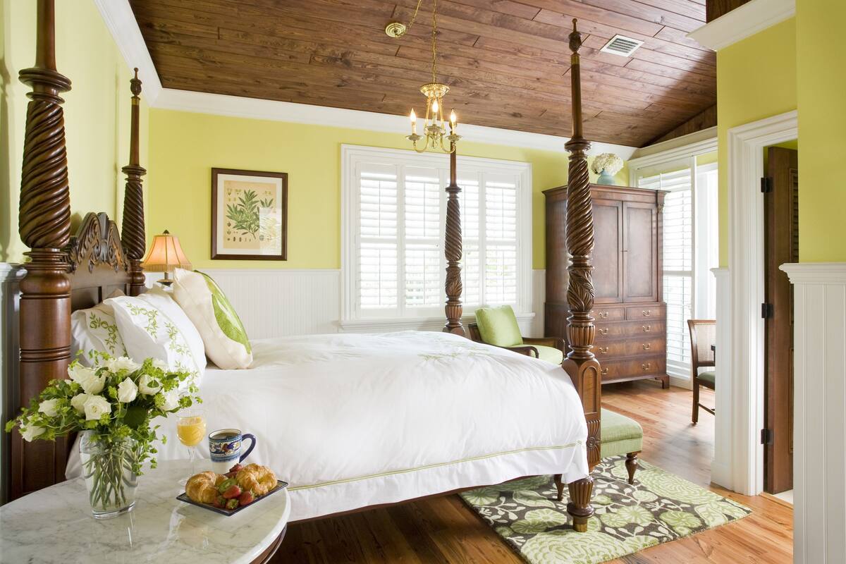 A bedroom with a four-poster bed, a chandelier, wooden flooring, and a green wall.
