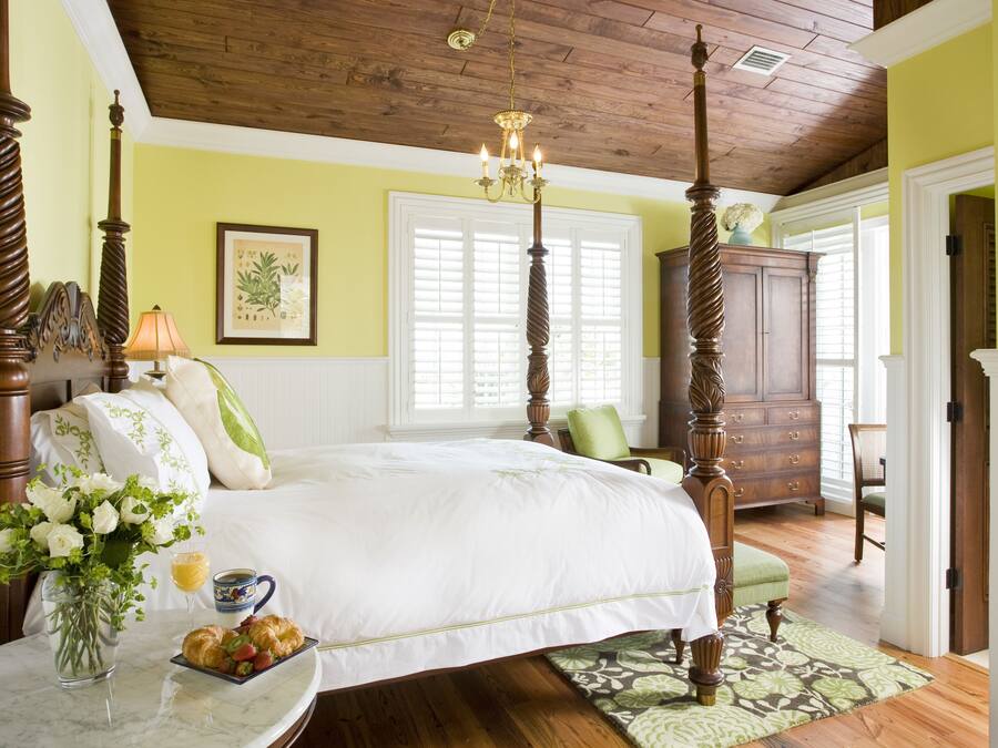 A bedroom with a four-poster bed, a chandelier, wooden flooring, and a green wall.