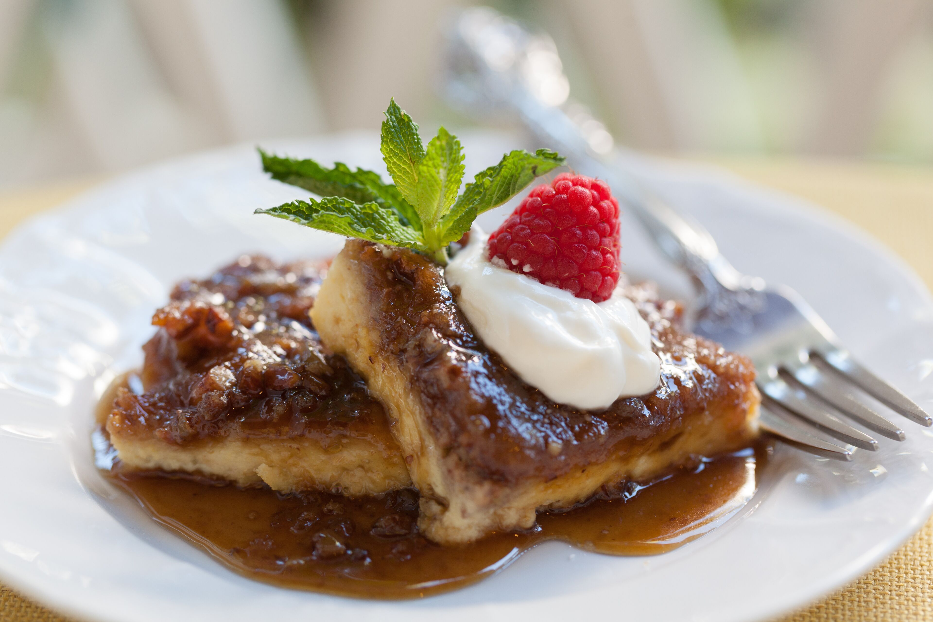 Un plato de postre con una porción de pastel cubierto de salsa, una cucharada de crema y una frambuesa.