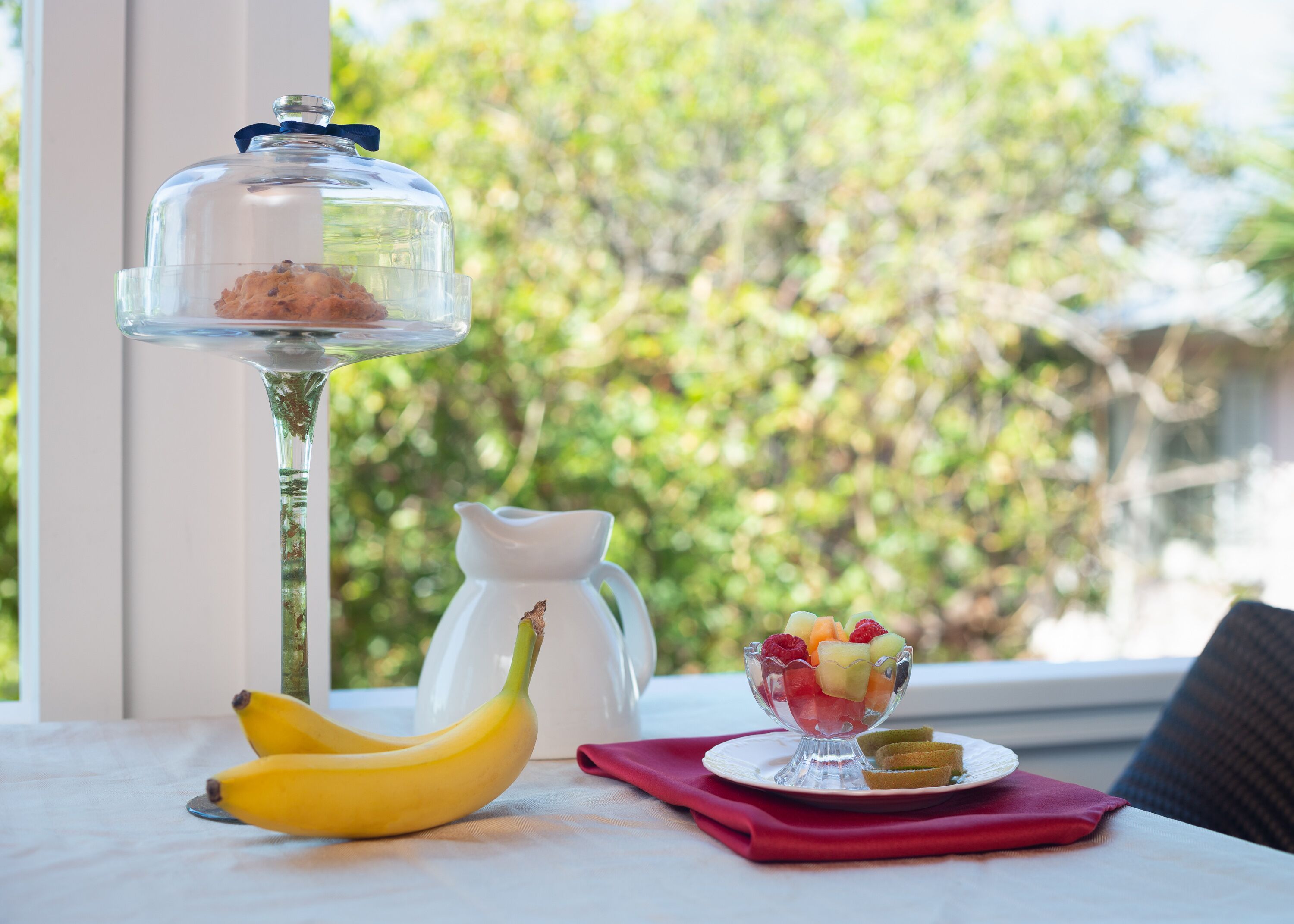 A table with a glass pitcher, a glass bowl of fruit, and bananas.