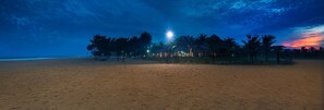Une plage au crépuscule, avec des palmiers et une structure illuminée.