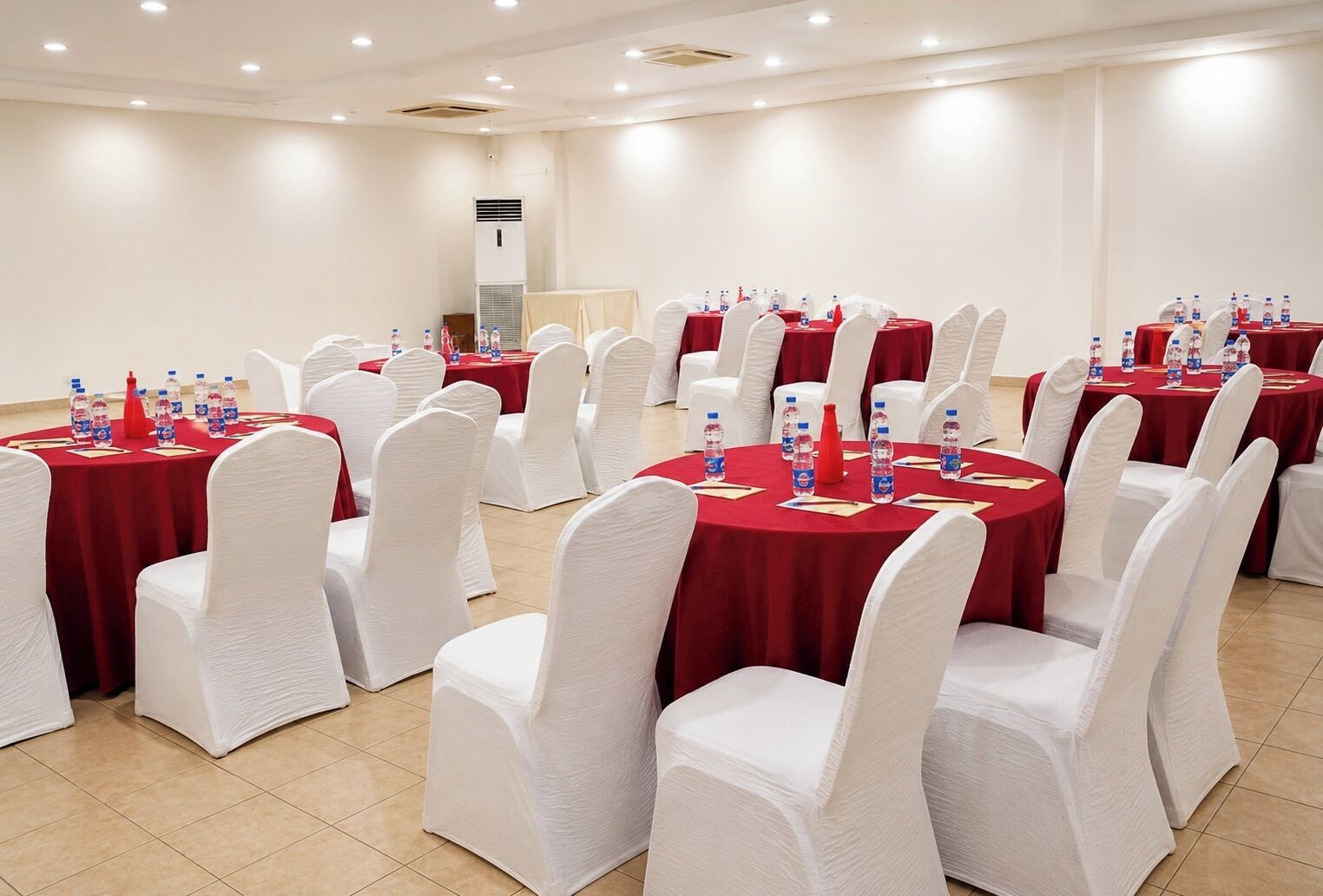A conference room with round tables, white chairs, and red tablecloths.