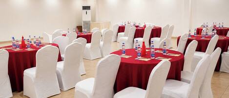 A conference room with round tables, white chairs, and red tablecloths.