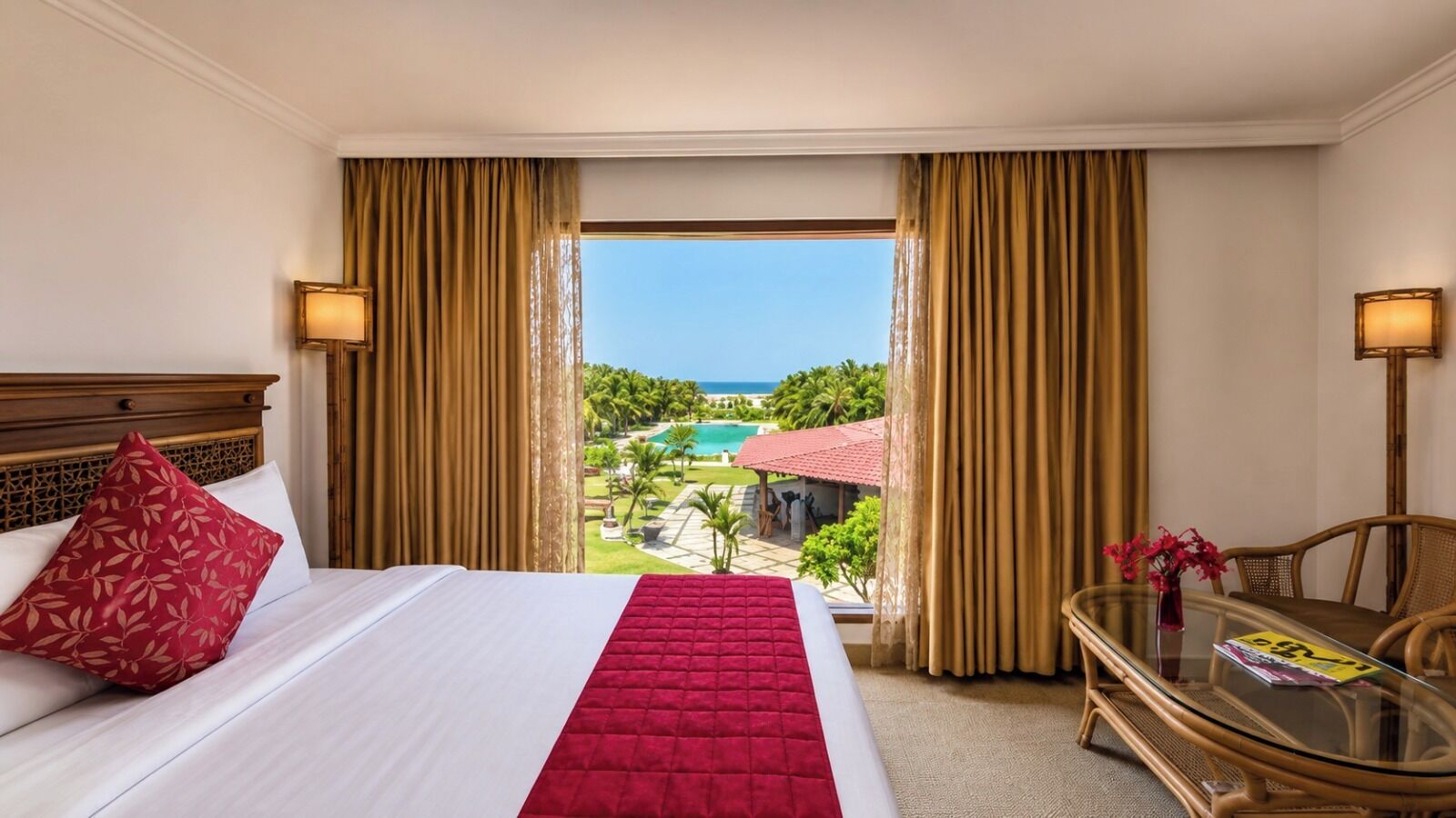 A hotel room with a bed, a glass table, and a view of a pool and greenery.