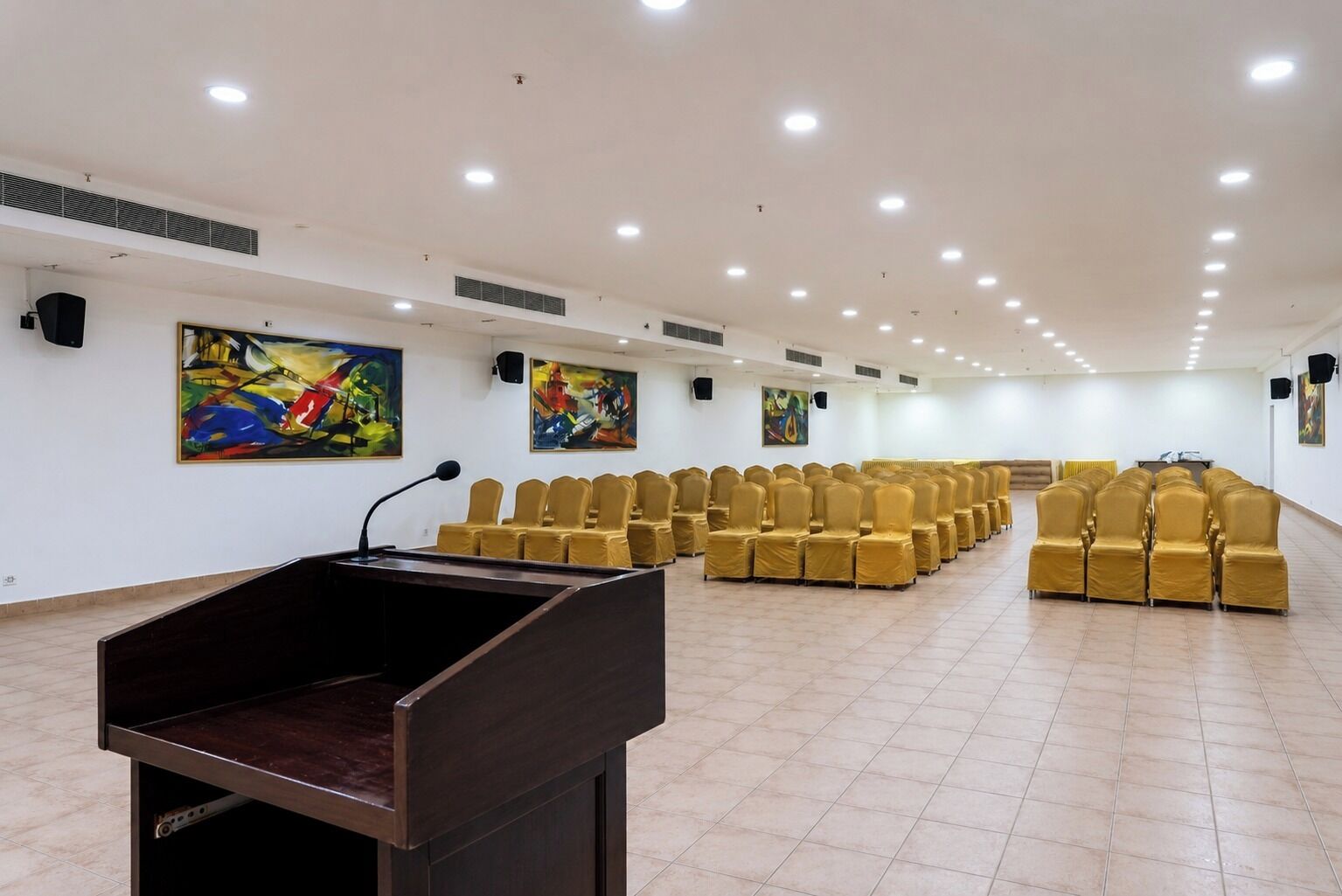A conference room with rows of chairs, a podium, and abstract paintings on the walls.