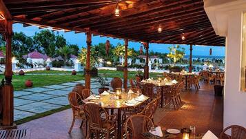 Un espace de restauration en plein air, avec des tables et des chaises en bois, agrémenté d’un jardin paysager en arrière-plan et offrant une vue sur la mer.
