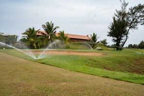 A grassy field with sprinklers and a building with a red roof in the background.