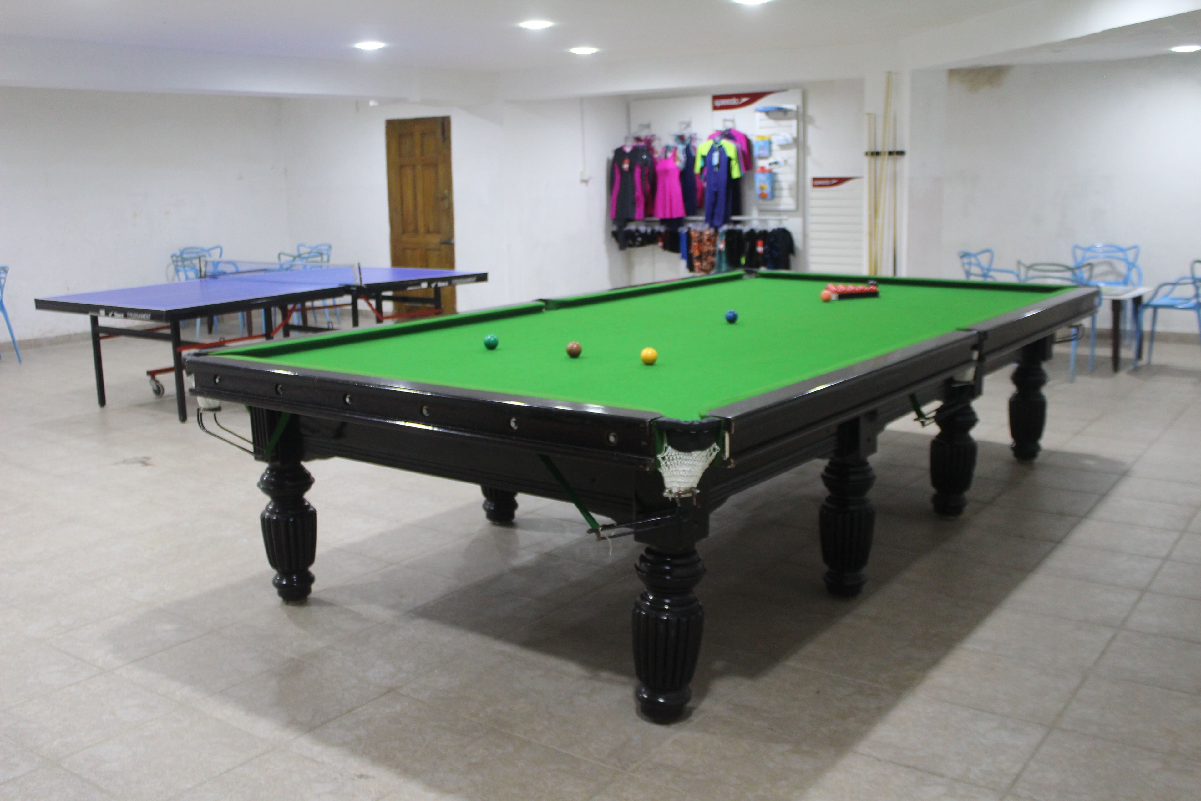 A billiards table with balls, a table tennis table, and chairs in a room with tiled flooring.